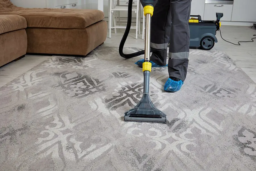 Person cleaning carpet with vacuum machine.