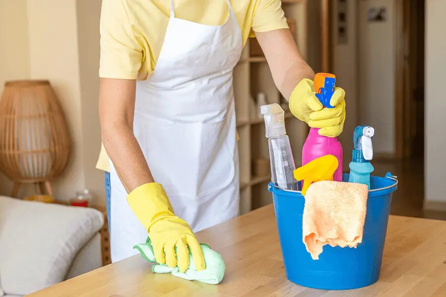 Person cleaning table with supplies in bucket.